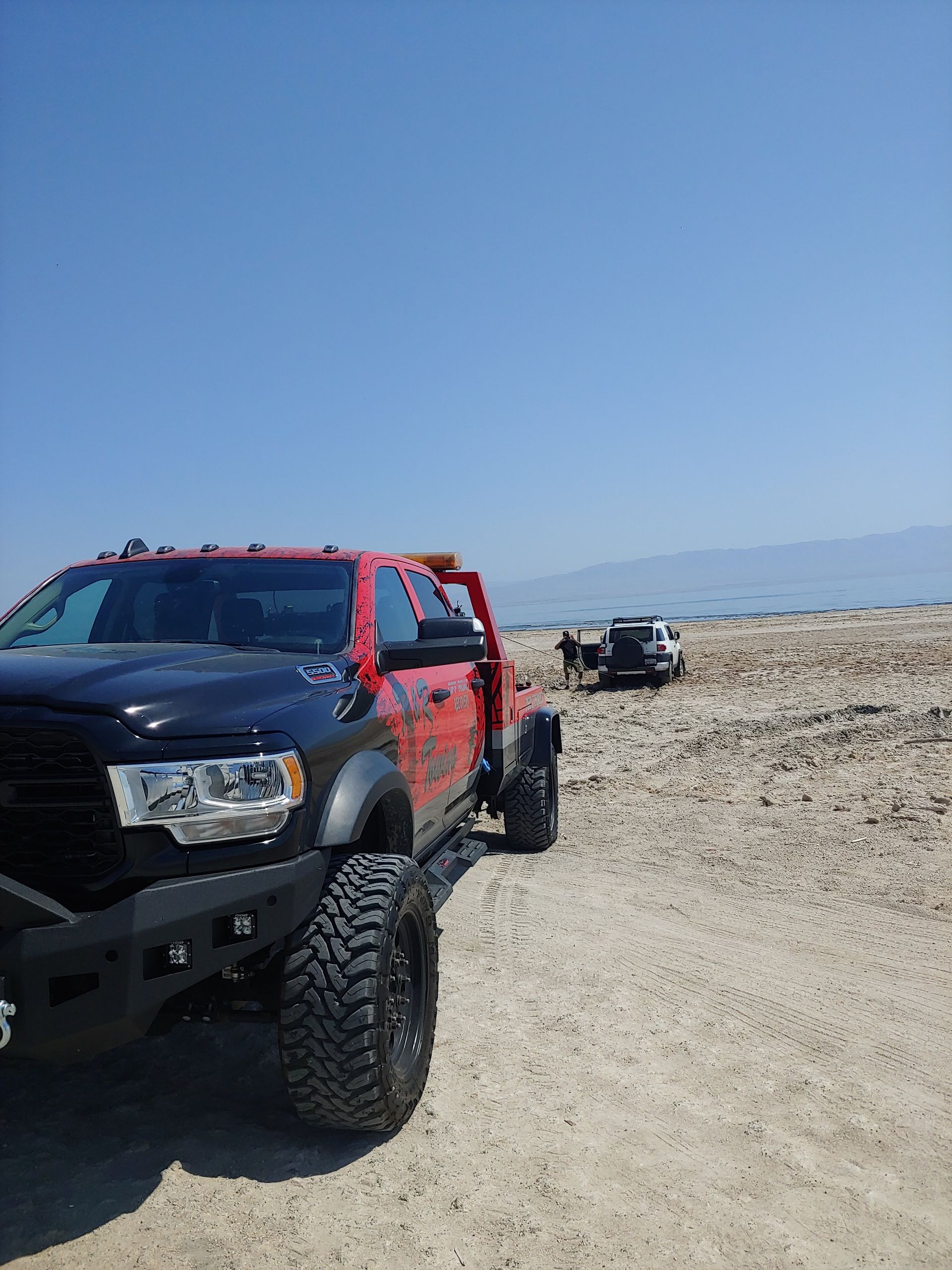 A red truck is parked in the sand on a beach.