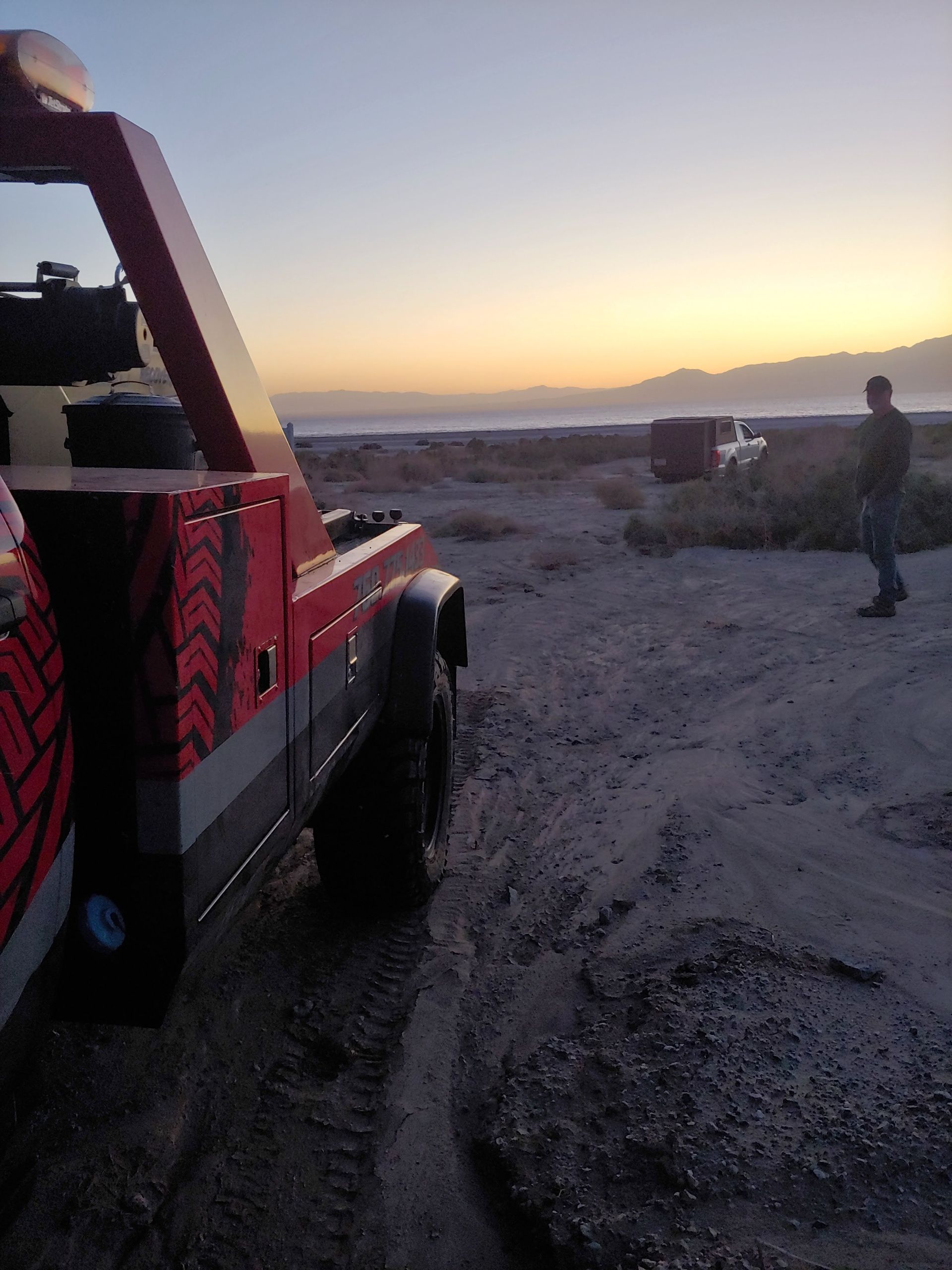 A red tow truck is parked on the side of a dirt road