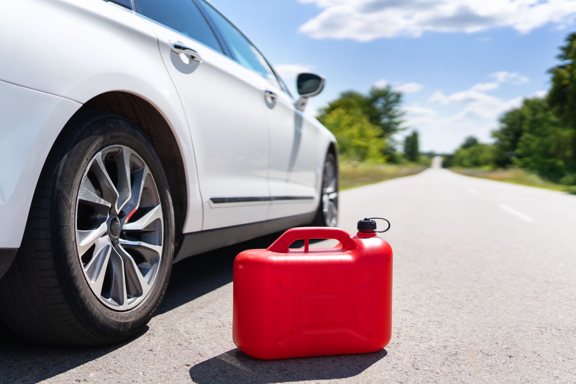 A red gas can is sitting next to a white car on the side of the road.