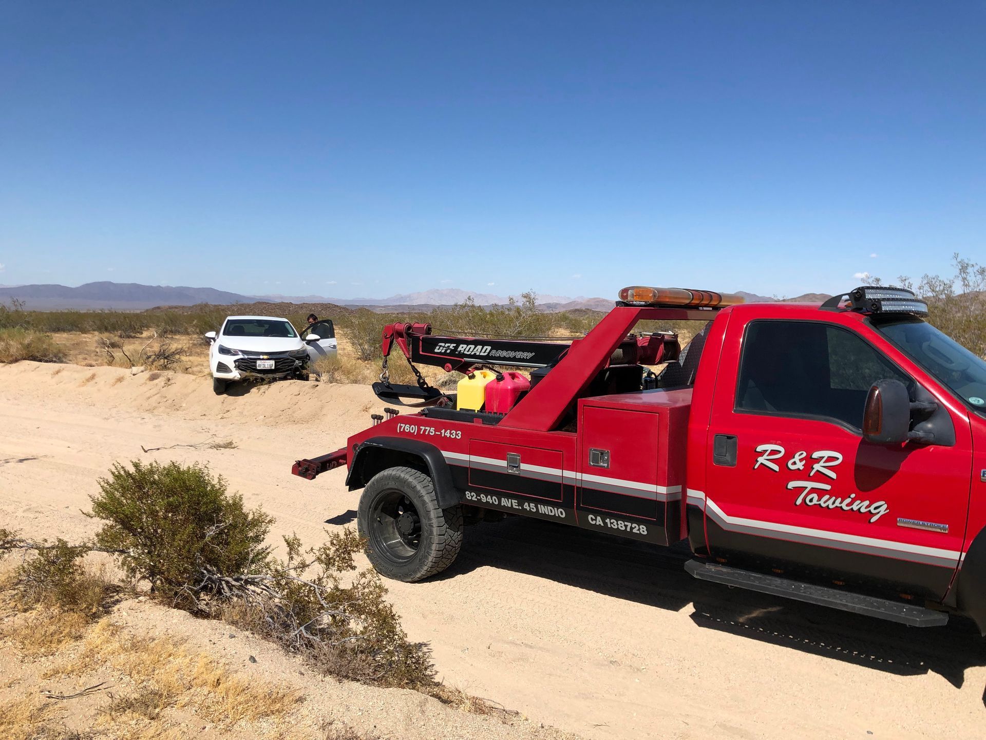 A red tow truck is towing a white car in the desert.