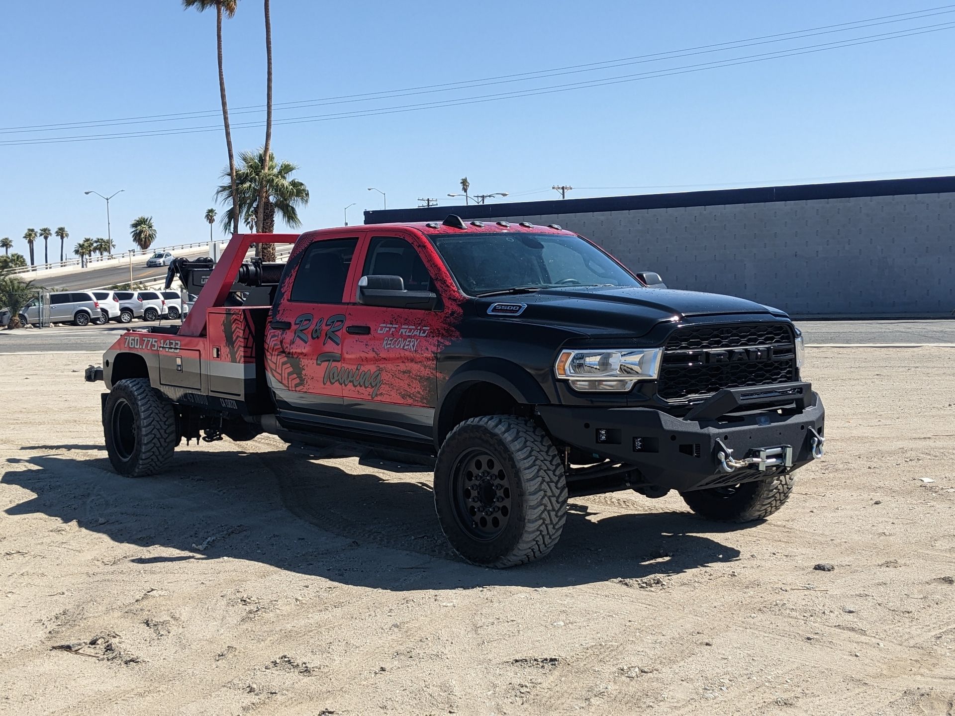 A red and black tow truck is parked in a dirt field.