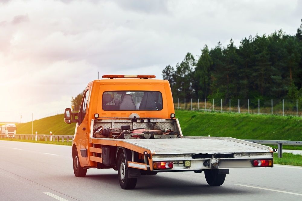 A Tow Truck is Driving Down a Highway With a Flat Bed — Trucking Crane Trucks in Gympie, QLD
