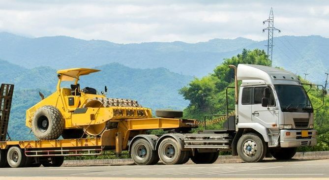 A Truck is Carrying a Yellow Bulldozer on a Trailer on a Highway — Trucking Crane Trucks in Gympie, QLD