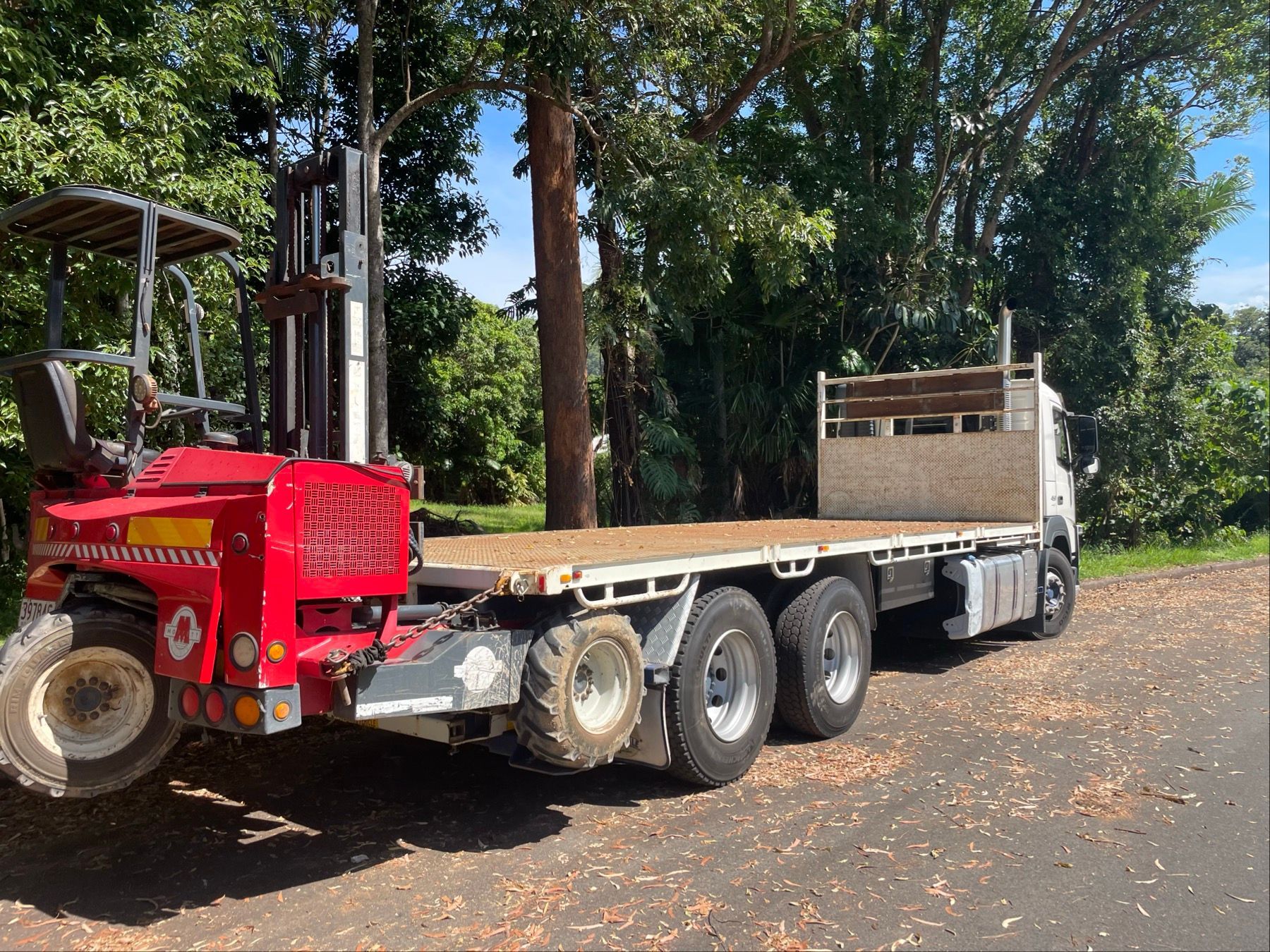 Red flatbed truck parked on a dirt road beside trees and greenery — Trucking Crane Trucks in Caboolture, QLD