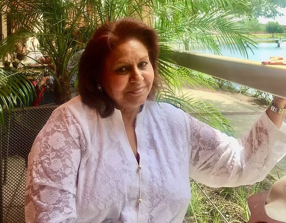 Woman in white lace top sits outdoors with lake in the background.