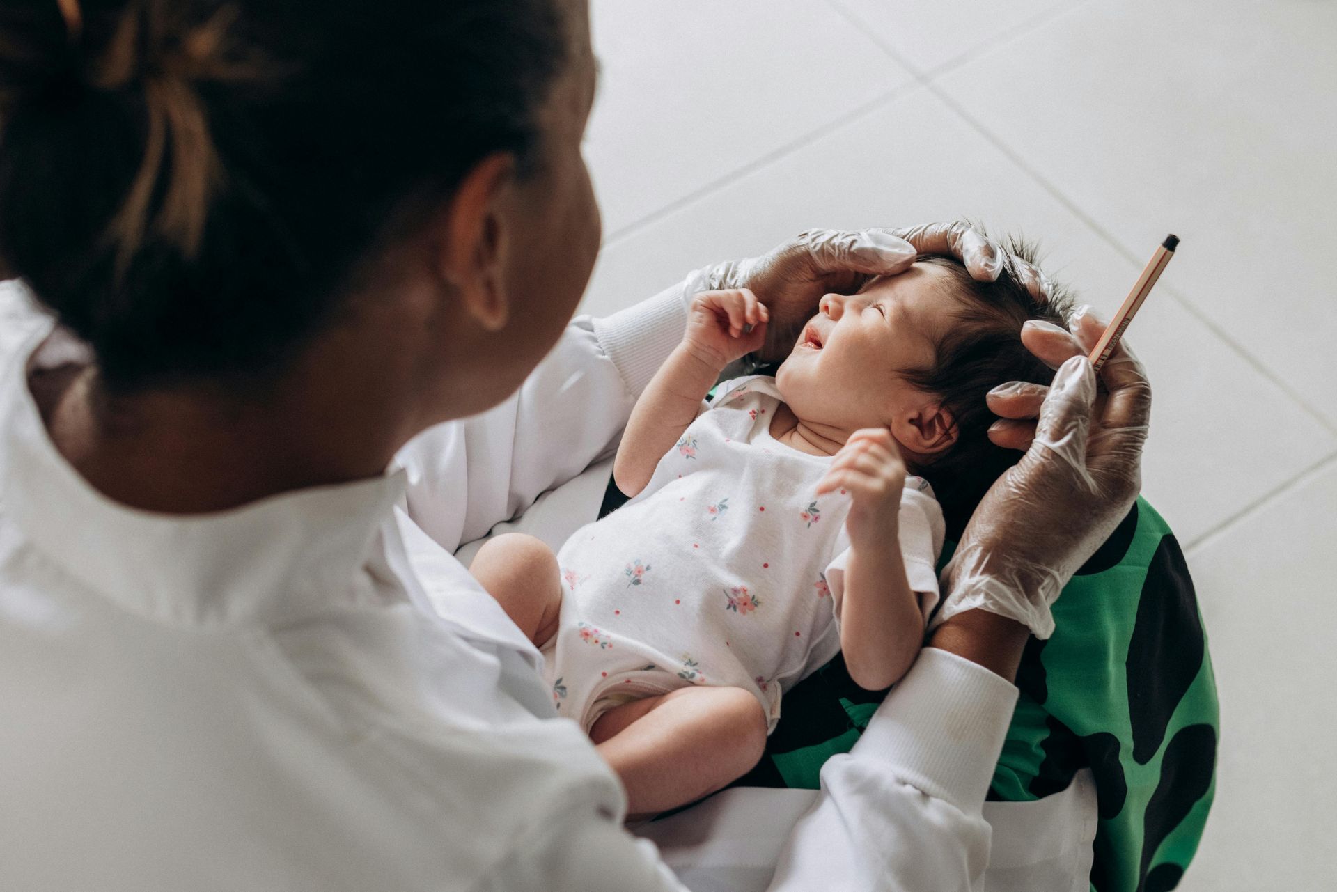 Person in gloves holding newborn baby, using a tool on baby's head. Baby looking up.