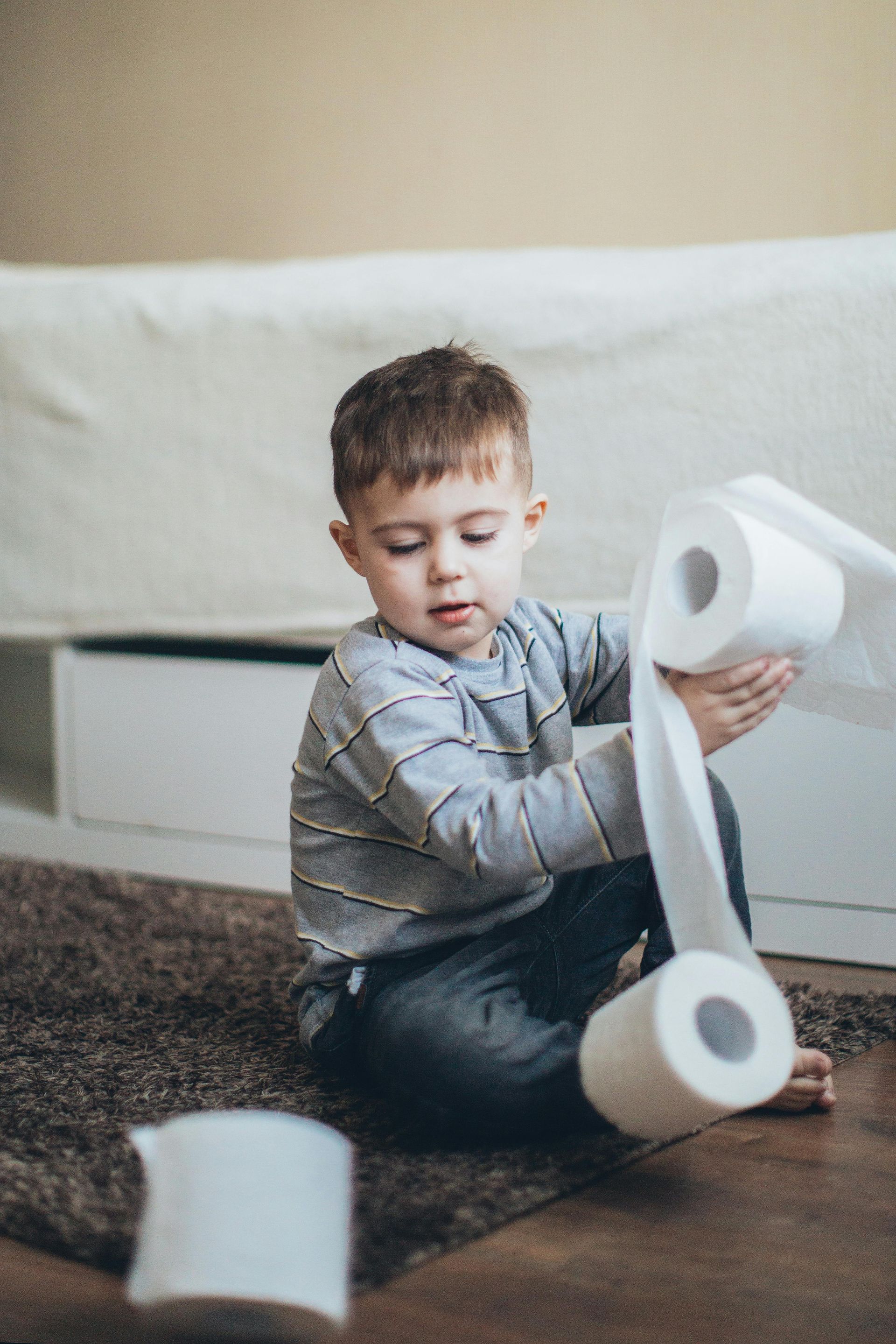 Young child sits on the floor playing with rolls of toilet paper.