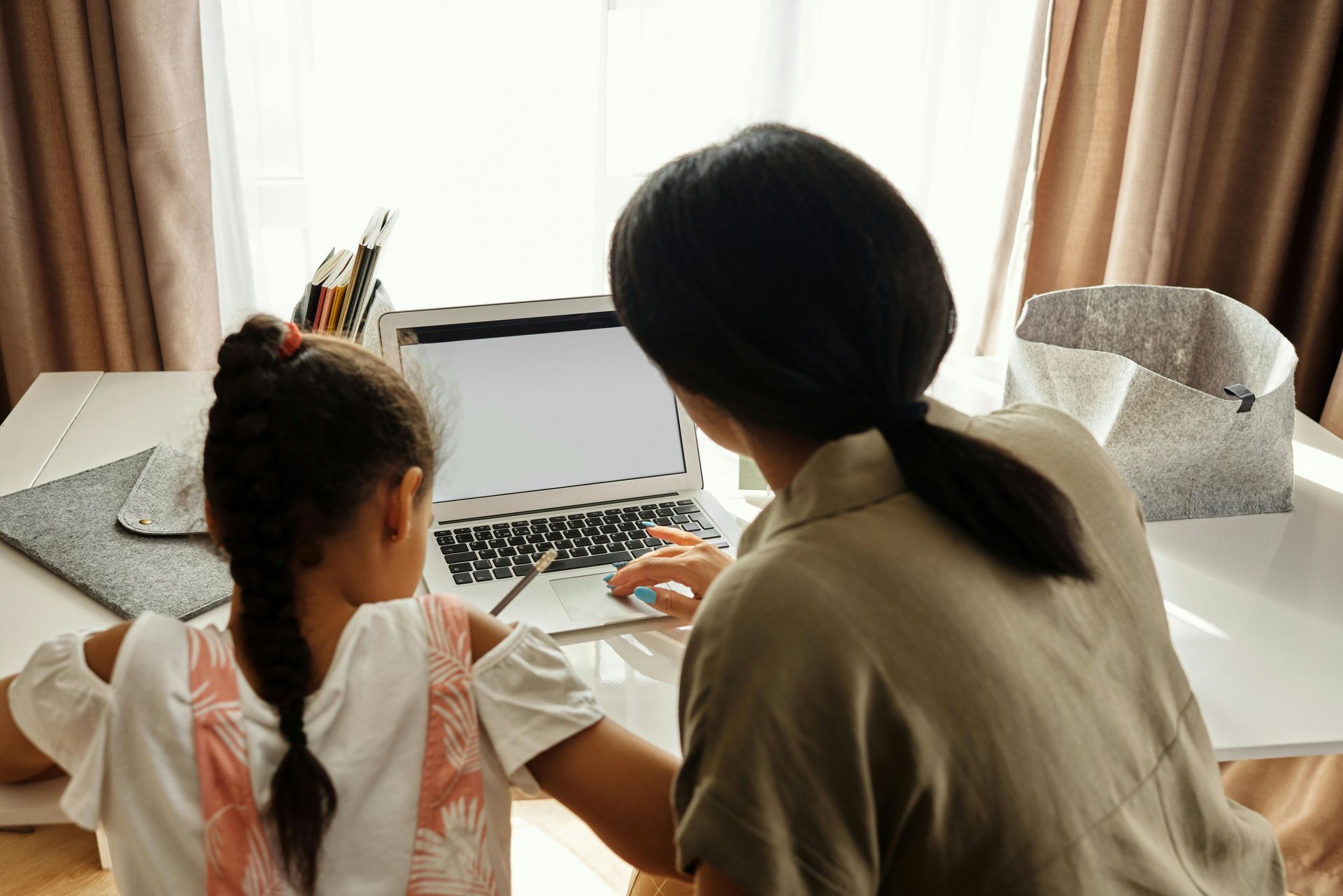 Woman and child looking at laptop screen at a desk in front of a window.