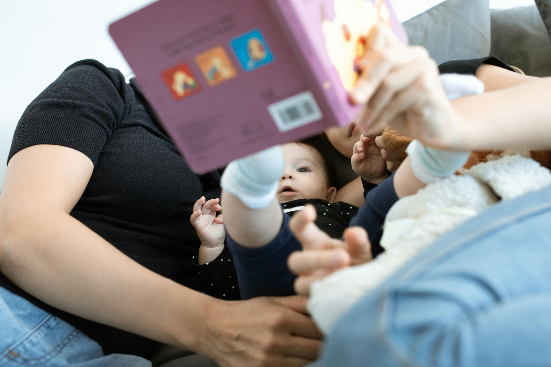 Person reads a book to a baby lying on their lap, in a living room.