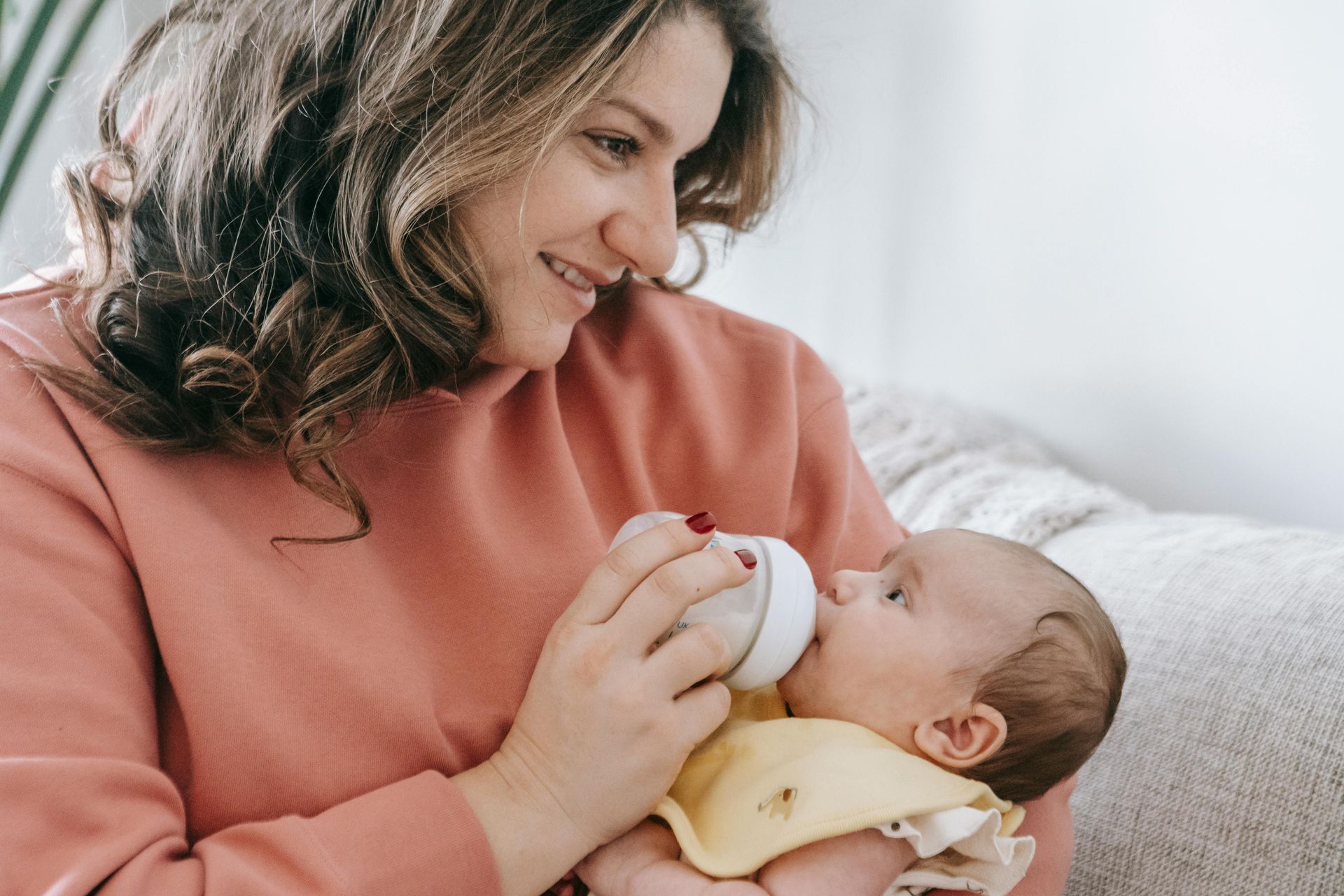 Woman feeding a baby with a bottle; both looking at each other, soft lighting, indoors.
