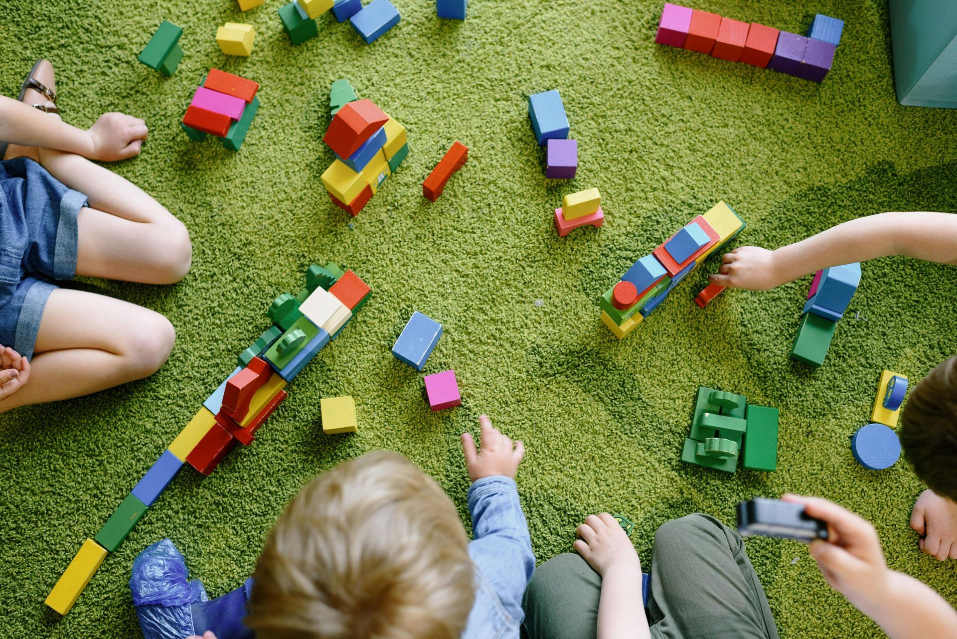 Children playing with colorful wooden blocks on a green carpet.