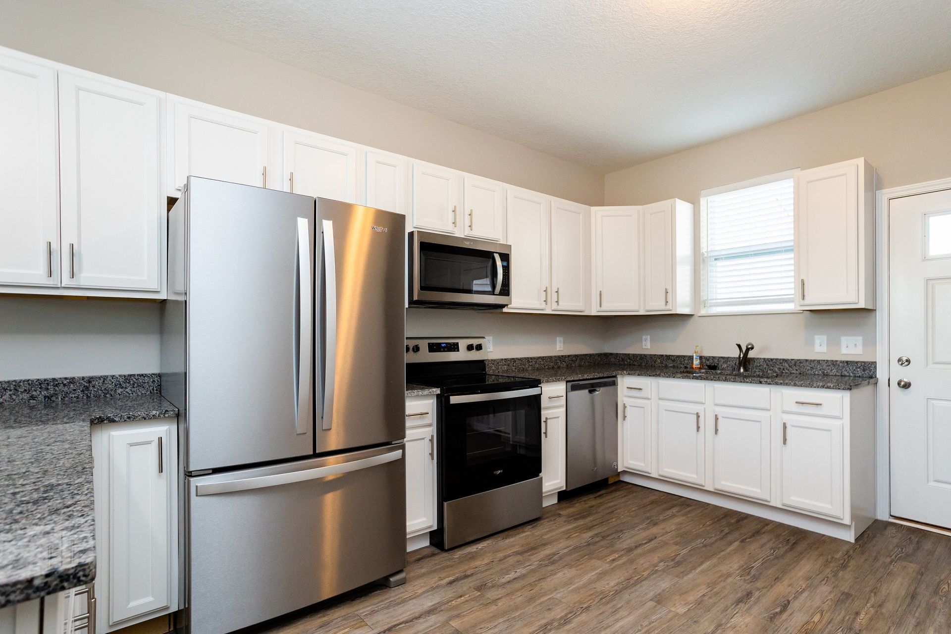 Bright kitchen with white cabinets, stainless steel appliances, and granite countertops.
