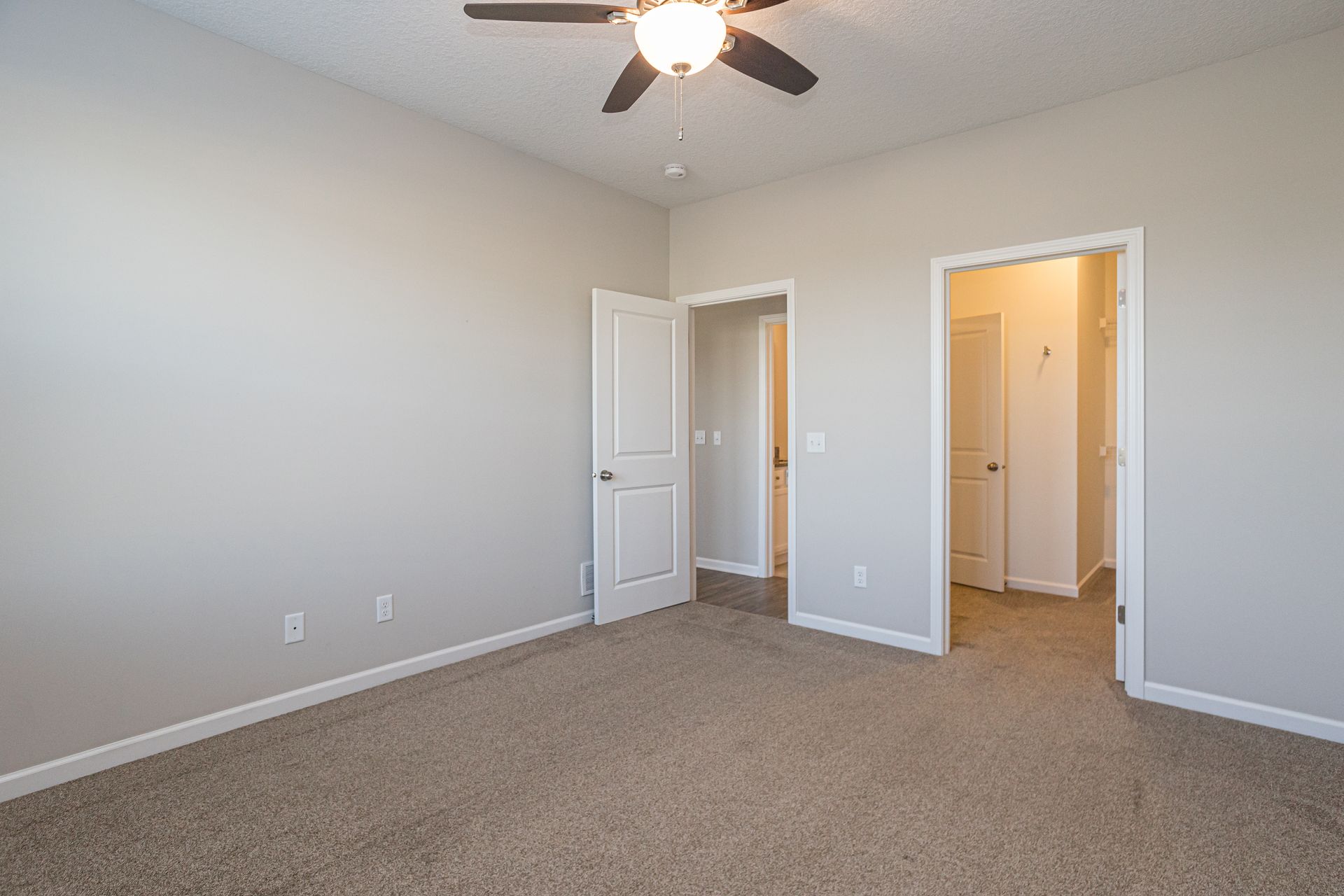 Empty bedroom with beige carpet, neutral walls, and open doors.