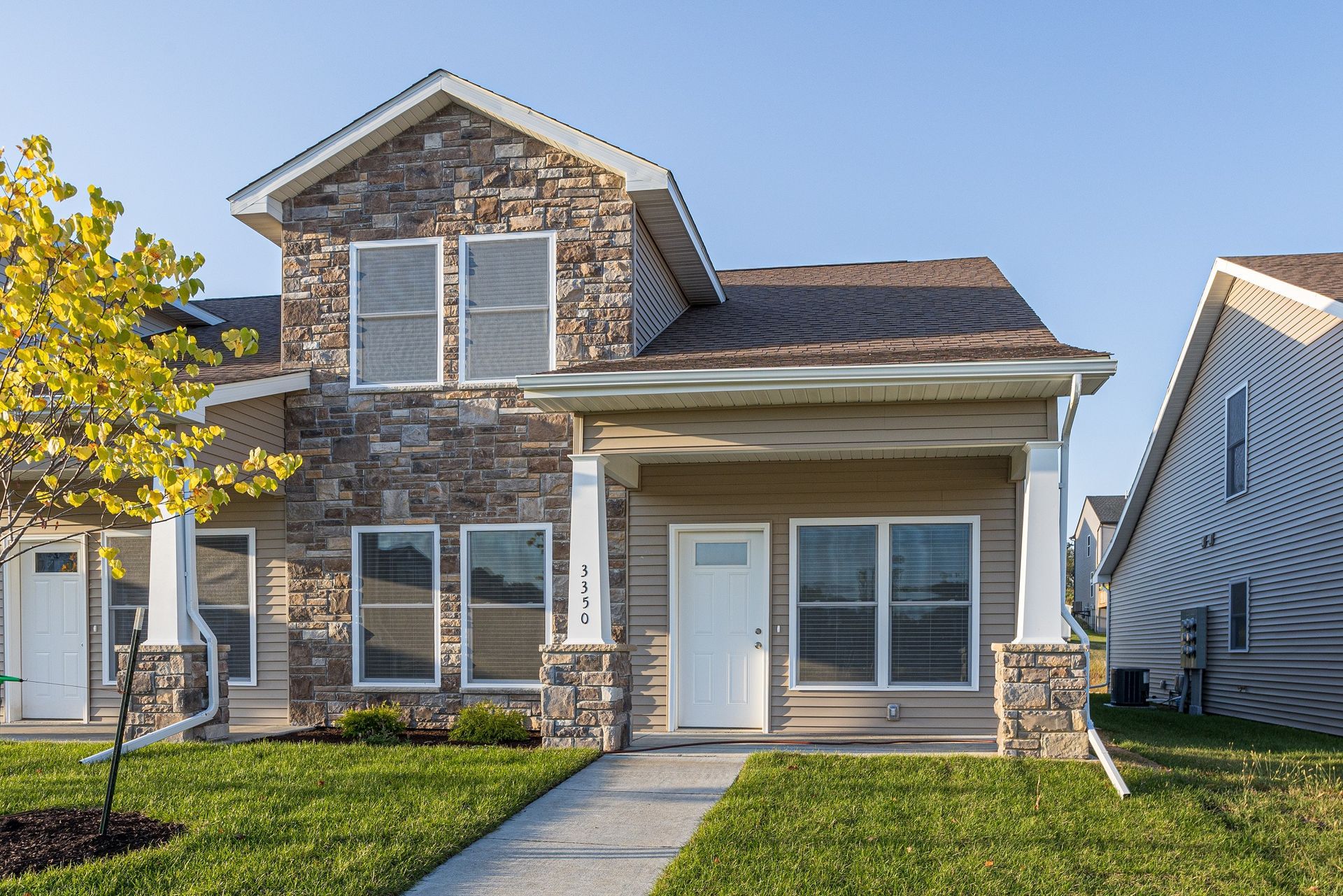 Two-story townhome with stone facade and beige siding, a white door, and a small porch.