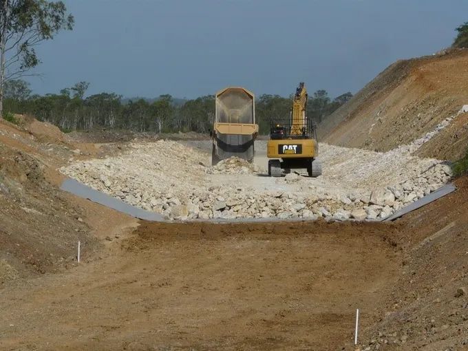 A Dump Truck Is Driving Down A Dirt Road Besides A Cat Excavator — Mike Barlow Earthmoving Pty Ltd in Rockhampton, QLD