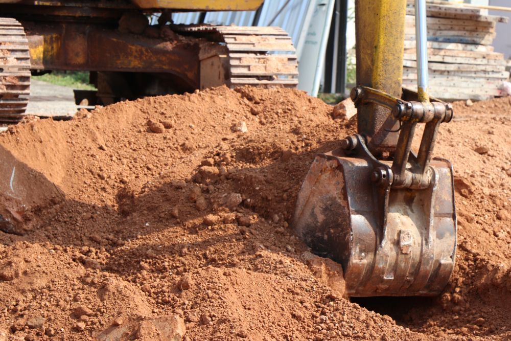 Excavator Bucket Digging Reddish Dirt at a Construction Site — Mike Barlow Earthmoving Pty Ltd in Rockhampton, QLD