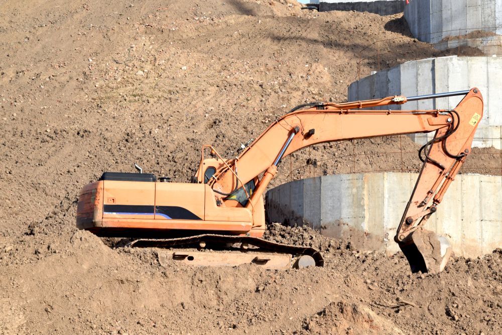 Orange Excavator Working in a Dirt Excavation Site Beside Concrete Retaining Walls — Mike Barlow Earthmoving Pty Ltd in Rockhampton, QLD
