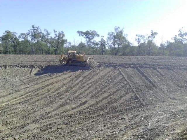 A Bulldozer Is Plowing a Dirt Field with Trees in The Background — Mike Barlow Earthmoving Pty Ltd in Rockhampton, QLD