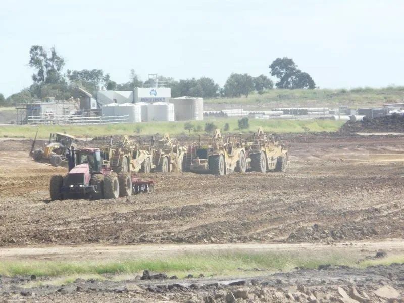 A Lot Of Excavators Driving In Row On Dirt Field — Mike Barlow Earthmoving Pty Ltd in Rockhampton, QLD