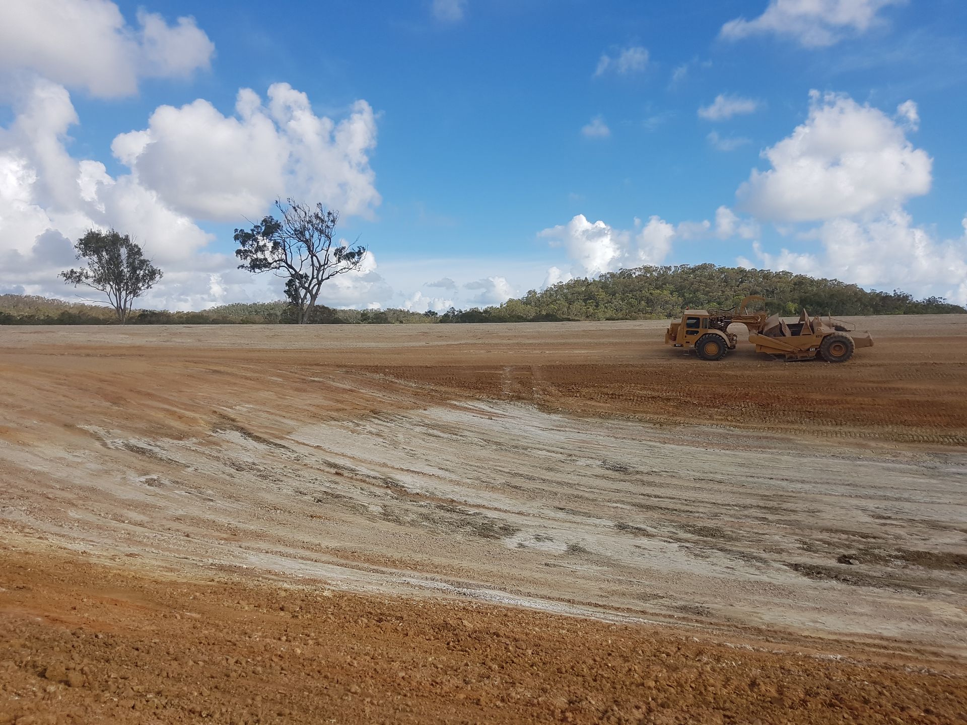 A Bulldozer Is Moving Dirt in A Field With Trees in The Background — Mike Barlow Earthmoving Pty Ltd in Yeppoon, QLD