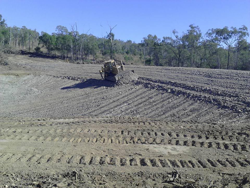 A Bulldozer Is Plowing a Dirt Field with Trees in The Background — Mike Barlow Earthmoving Pty Ltd in Rockhampton, QLD