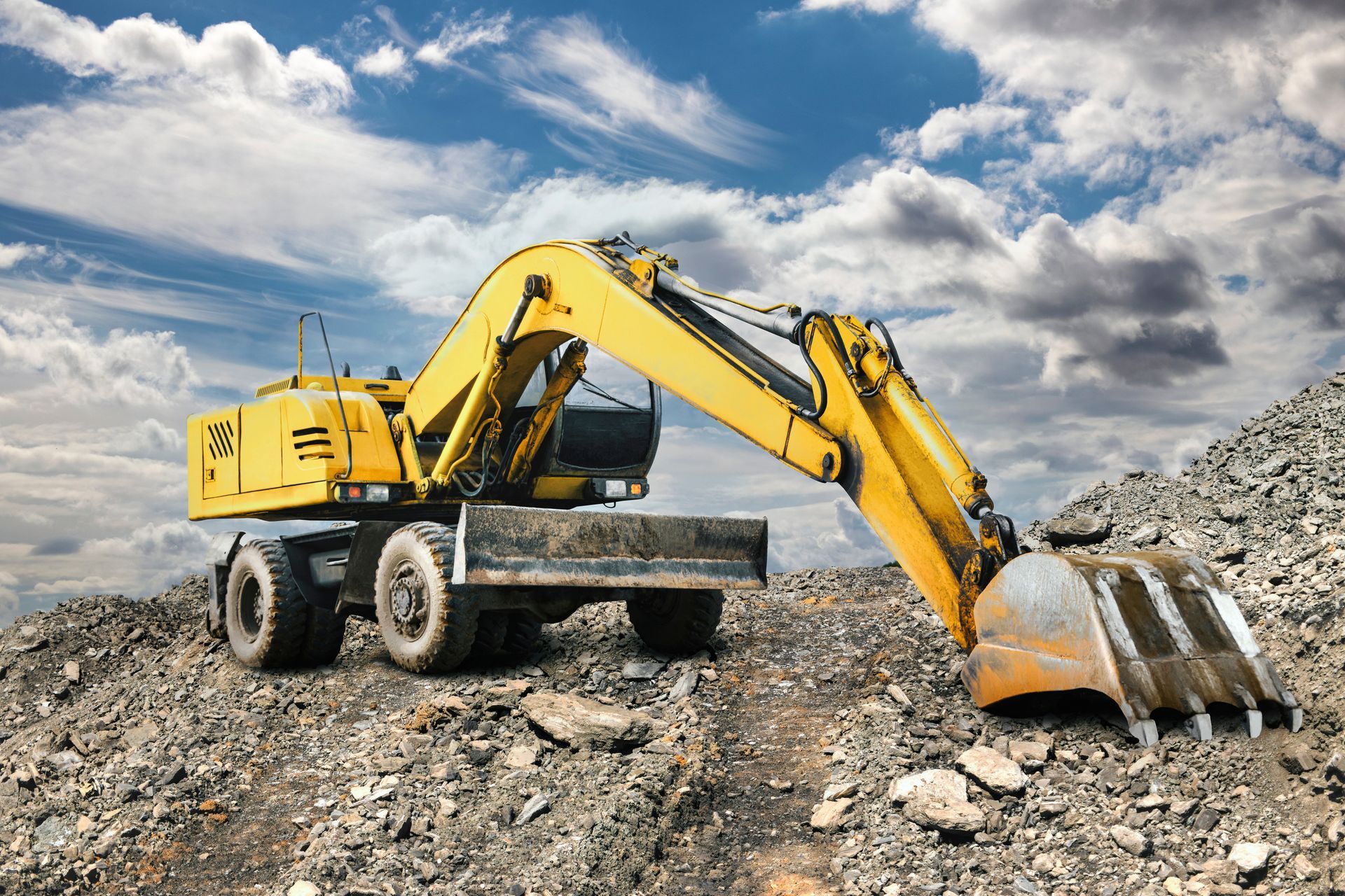 Yellow Excavator on a Rocky Construction Site Under a Cloudy Blue Sky — Mike Barlow Earthmoving Pty Ltd in Rockhampton, QLD