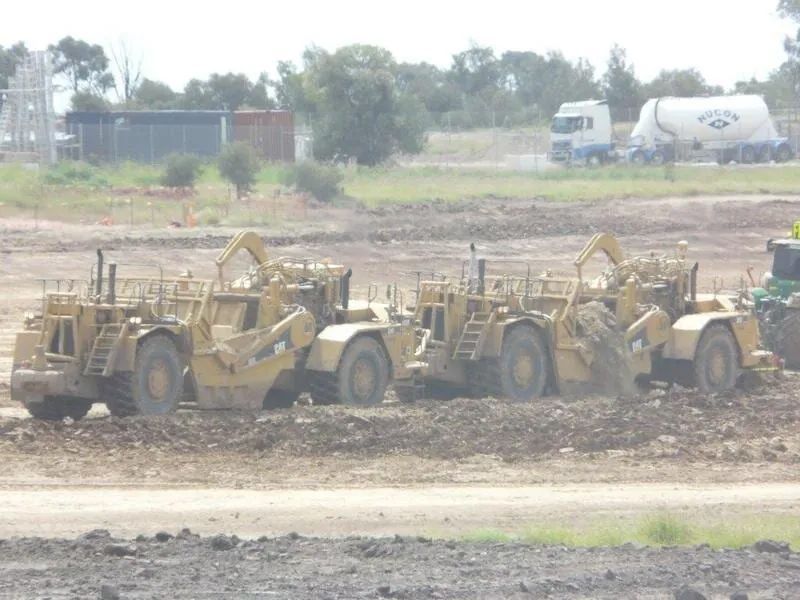 Row Of Excavator On Dirt Ground With Trailer Truck In Background — Mike Barlow Earthmoving Pty Ltd in Rockhampton, QLD