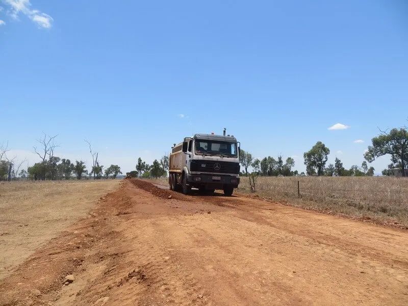 A Dump Truck Is Driving Down a Dirt Road — Mike Barlow Earthmoving Pty Ltd in Central Highlands, QLD