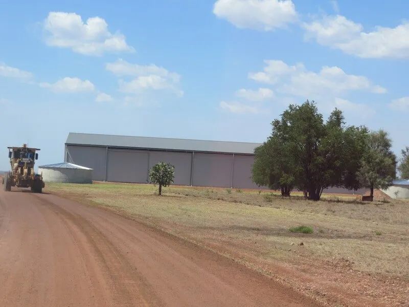 A Tractor Is Driving Down a Dirt Road in Front of A Building — Mike Barlow Earthmoving Pty Ltd in Central Highlands, QLD