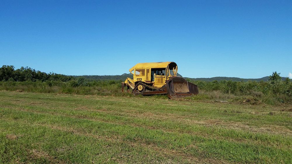 A Yellow Bulldozer Is Driving Through a Grassy Field — Mike Barlow Earthmoving Pty Ltd in Rockhampton, QLD