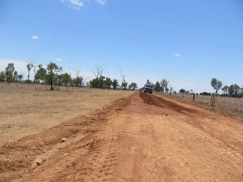 A Car Is Driving Down a Dirt Road in The Middle of A Field — Mike Barlow Earthmoving Pty Ltd in Central Highlands, QLD