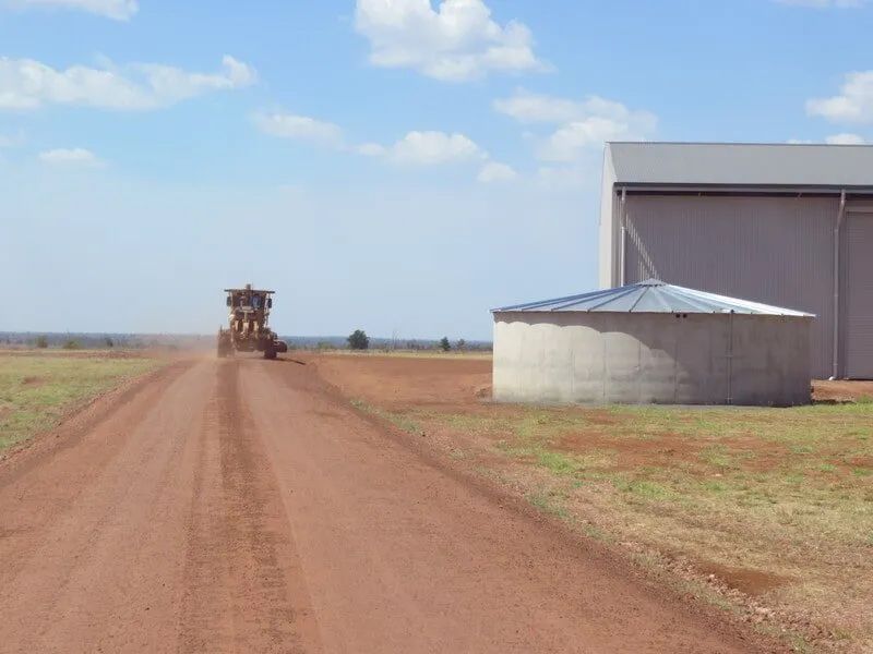 Excavator Passing On Dirt Road Besides A Shed — Mike Barlow Earthmoving Pty Ltd in Rockhampton, QLD