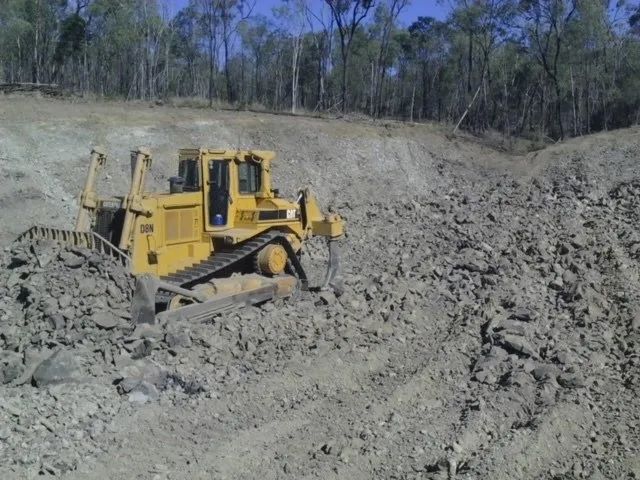 Yellow Bulldozer Pushing Dirt Pile To Clean The Land — Mike Barlow Earthmoving Pty Ltd in Rockhampton, QLD