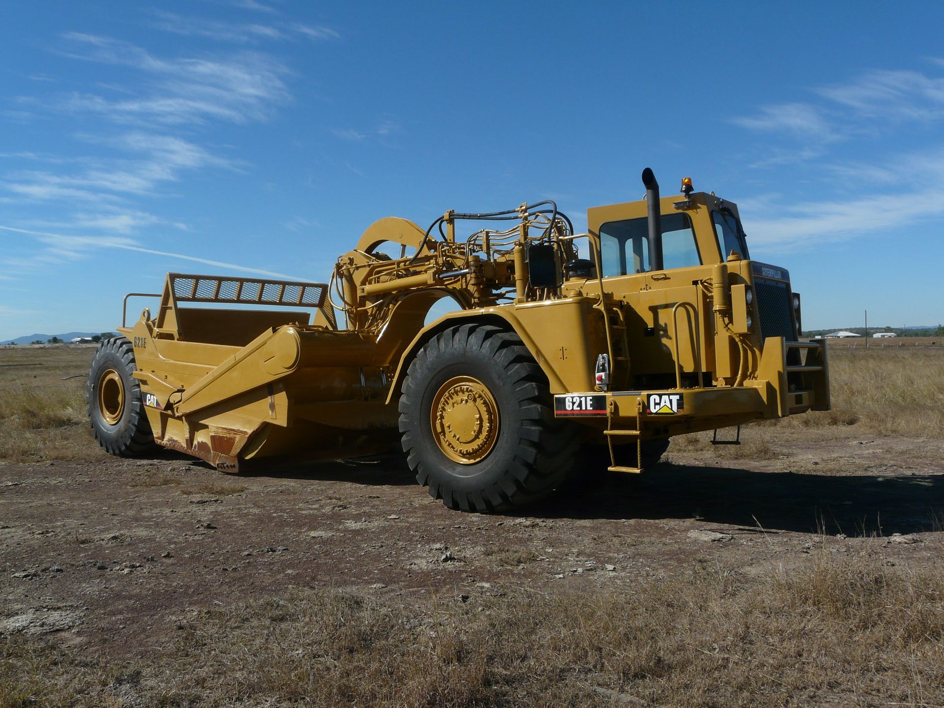 A Large Yellow Tractor Drives Along A Dirt Road Beside A Pile of Rocks — Mike Barlow Earthmoving Pty Ltd in Rockhampton, QLD