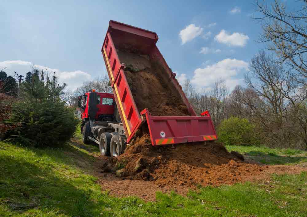 A Red Dump Truck Is Dumping Dirt Into A Field — Mike Barlow Earthmoving Pty Ltd in Rockhampton, QLD
