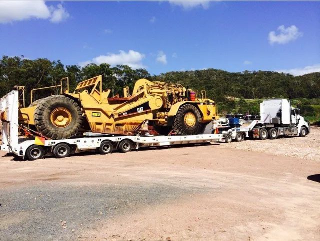 A Large Yellow Tractor Is Being Transported on A Trailer — Mike Barlow Earthmoving Pty Ltd in Yeppoon, QLD