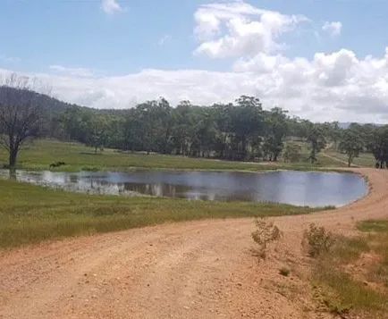 A Dirt Road Leading to A Small Pond in The Middle of A Field — Mike Barlow Earthmoving Pty Ltd in Yeppoon, QLD