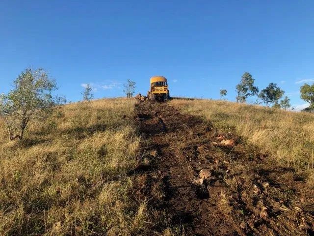 A Bulldozer Is Driving Down A Dirt Road On Top Of A Grassy Hill — Mike Barlow Earthmoving Pty Ltd in Rockhampton, QLD
