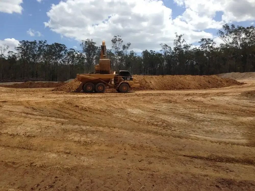 A Bulldozer Is Moving Dirt in A Field with Trees in The Background — Mike Barlow Earthmoving Pty Ltd in Rockhampton, QLD