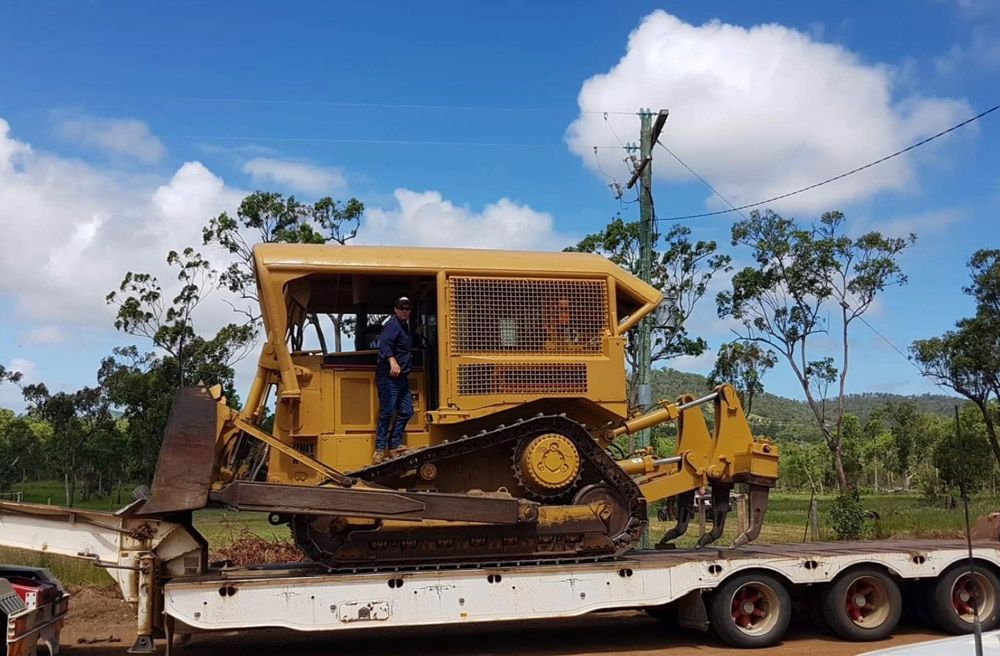Yellow Heavy Excavator Is Digging a Hole In A Muddy Field — Mike Barlow Earthmoving Pty Ltd in Rockhampton, QLD
