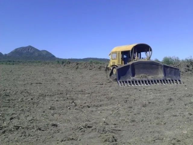 A Bulldozer Is Plowing a Dirt Field with Mountains in The Background — Mike Barlow Earthmoving Pty Ltd in Gladstone, QLD
