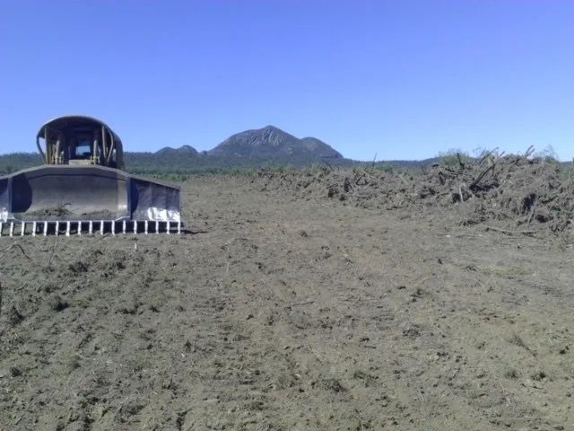 A Bulldozer Is Plowing a Dirt Field with Mountains in The Background — Mike Barlow Earthmoving Pty Ltd in Gladstone, QLD
