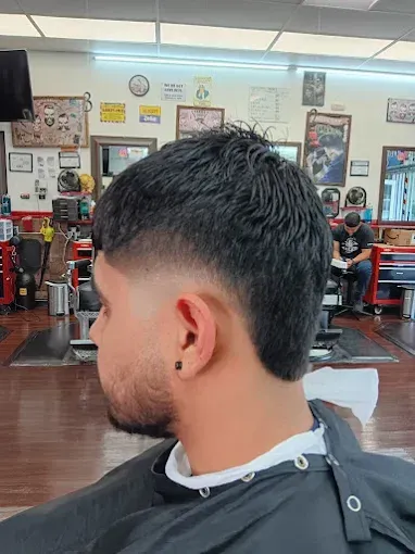 Man with a faded haircut at a barbershop, looking to the side. Dark hair with a bald fade, visible earring.