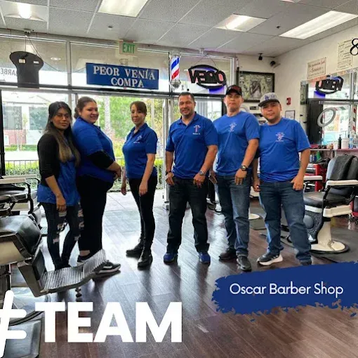 A group of six people in blue shirts stand in a barbershop, posing for a photo. The barbershop has chairs and mirrors.