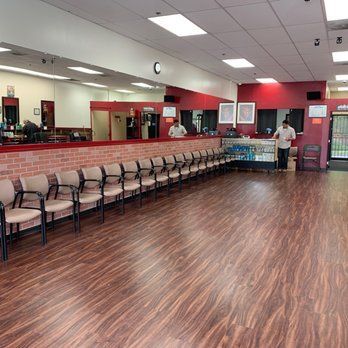 Interior of a barbershop with brick wall, mirrors, waiting chairs, and a person standing near a counter.