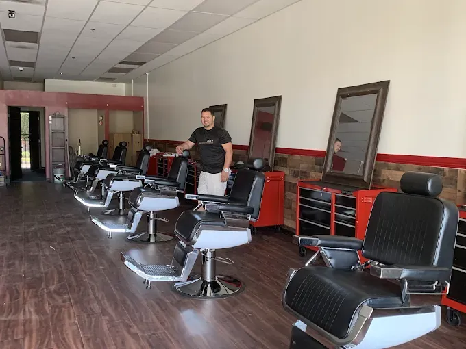 A barber shop interior with several black barber chairs in a row. A barber stands near the chairs.