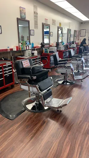 Barber shop interior with several barber chairs, mirrors, and tools arranged in a row. The floor is wood, and the walls are white.