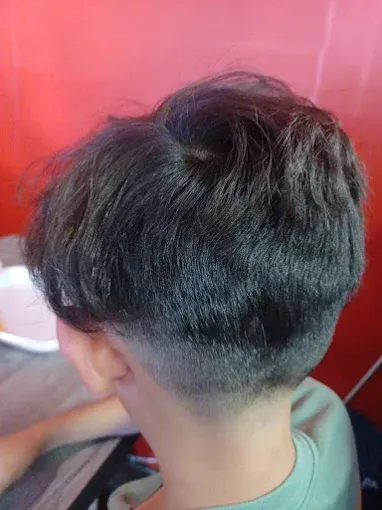 Back view of a person with a dark-haired bowl cut, with faded shaved sides and a red background.