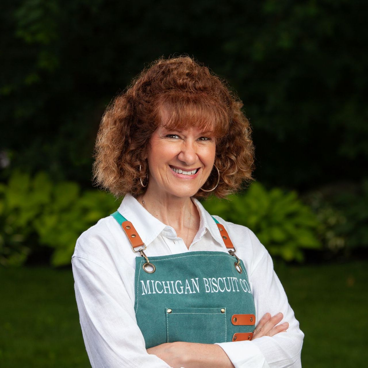 A woman wearing a Michigan Biscuit Co. apron is smiling with her arms crossed.