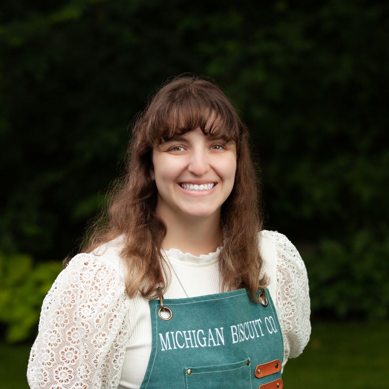 A woman wearing a Michigan Biscuit Co. apron over a white shirt is smiling for the camera.